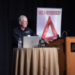 Photographers Of Las Vegas - Event Photography - Man speaking on stage South Point Need a Repossessor? Red triangle