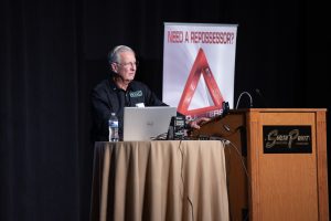 Photographers Of Las Vegas - Event Photography - Man speaking on stage South Point Need a Repossessor? Red triangle