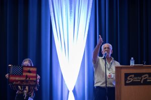 Photographers Of Las Vegas - Event Photography - South point stage blue drapery man speaking microphone woman holding united we stand sign